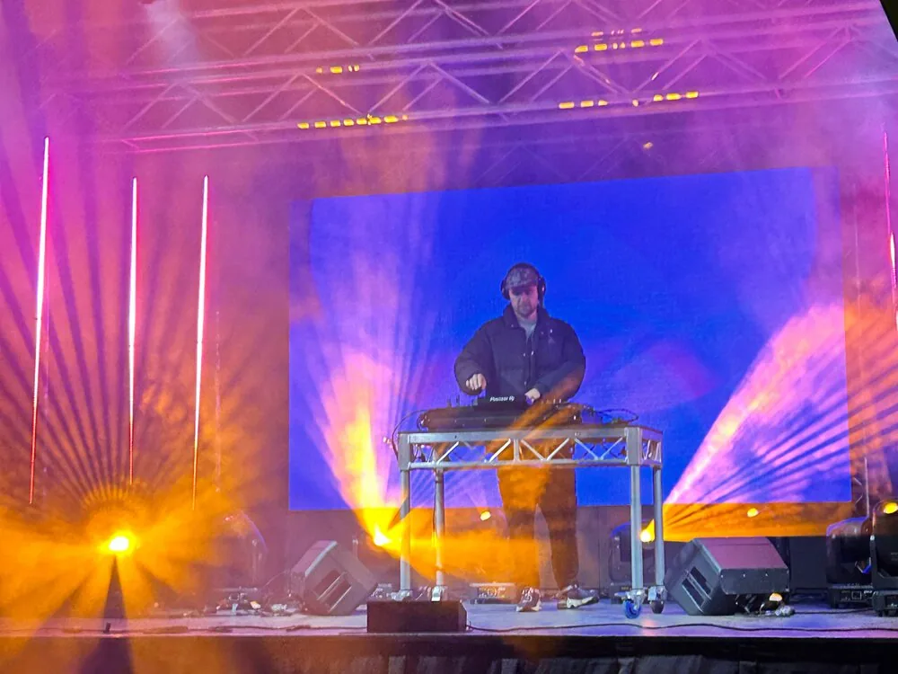 A DJ performing on a lit stage with coloured lights at a live event